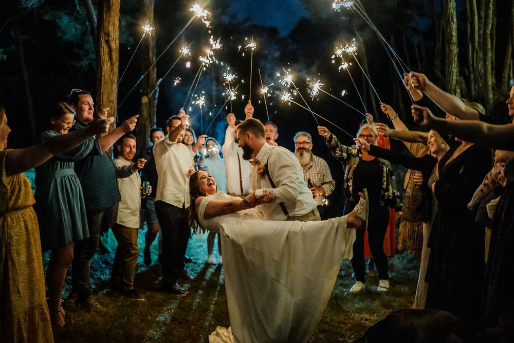 Guests hold sparklers as the groom dips the bride at a backyard wedding reception
