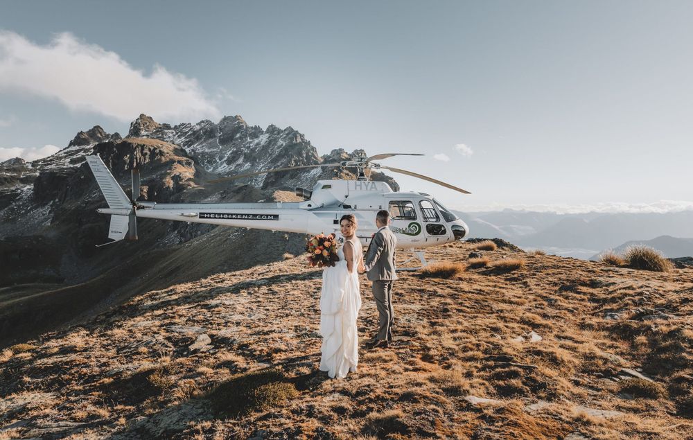 Bride and groom beside a helicopter on an alpine ridge during a Queenstown heli elopement