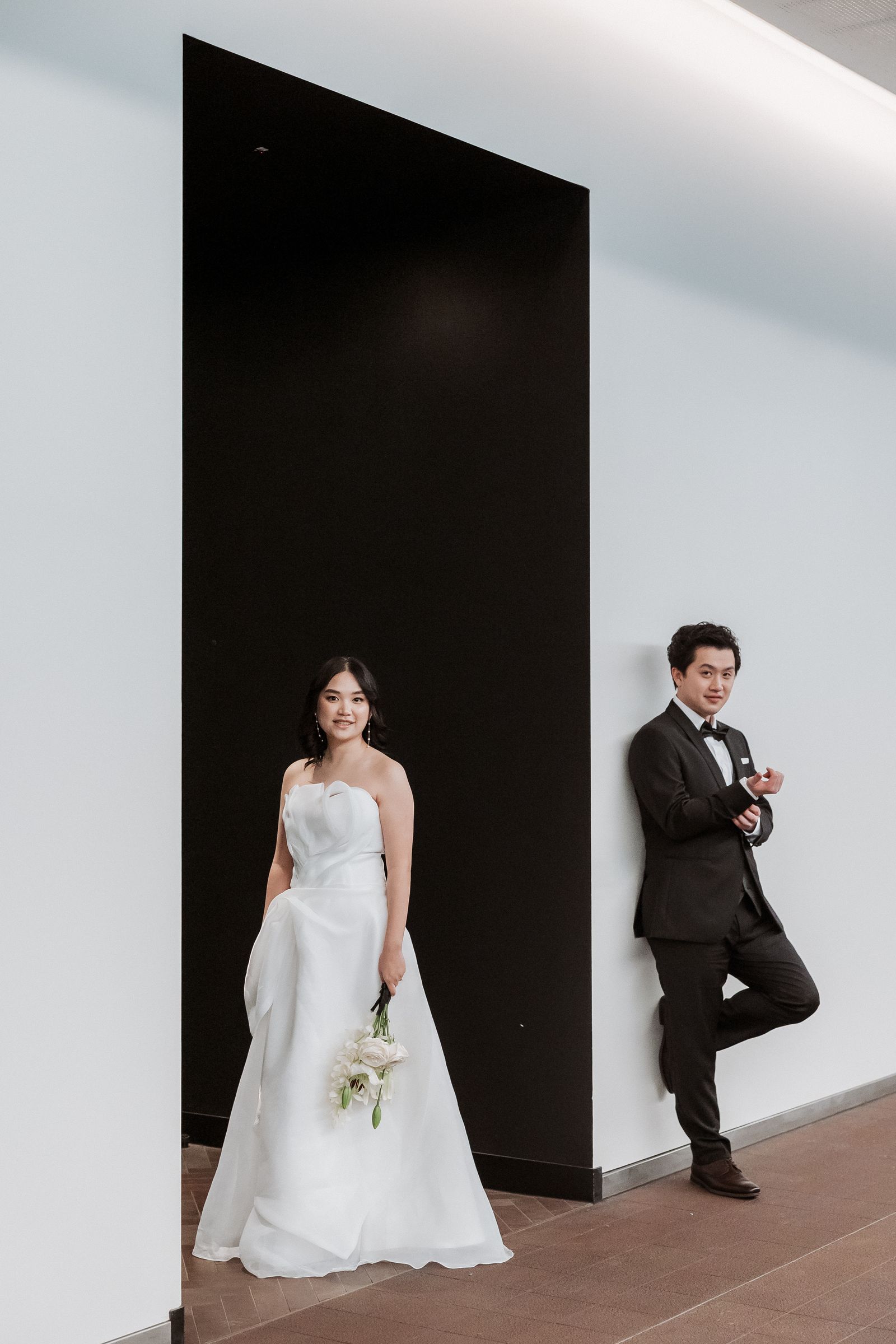 Bride and groom against a black panel and white wall in a modern Auckland interior