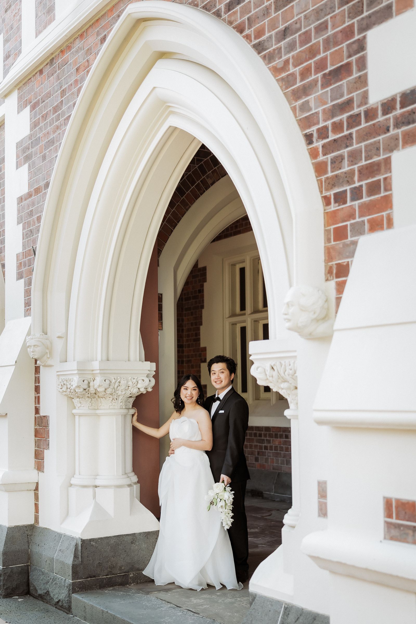 Bride and groom framed in a gothic brick and stone archway in Auckland