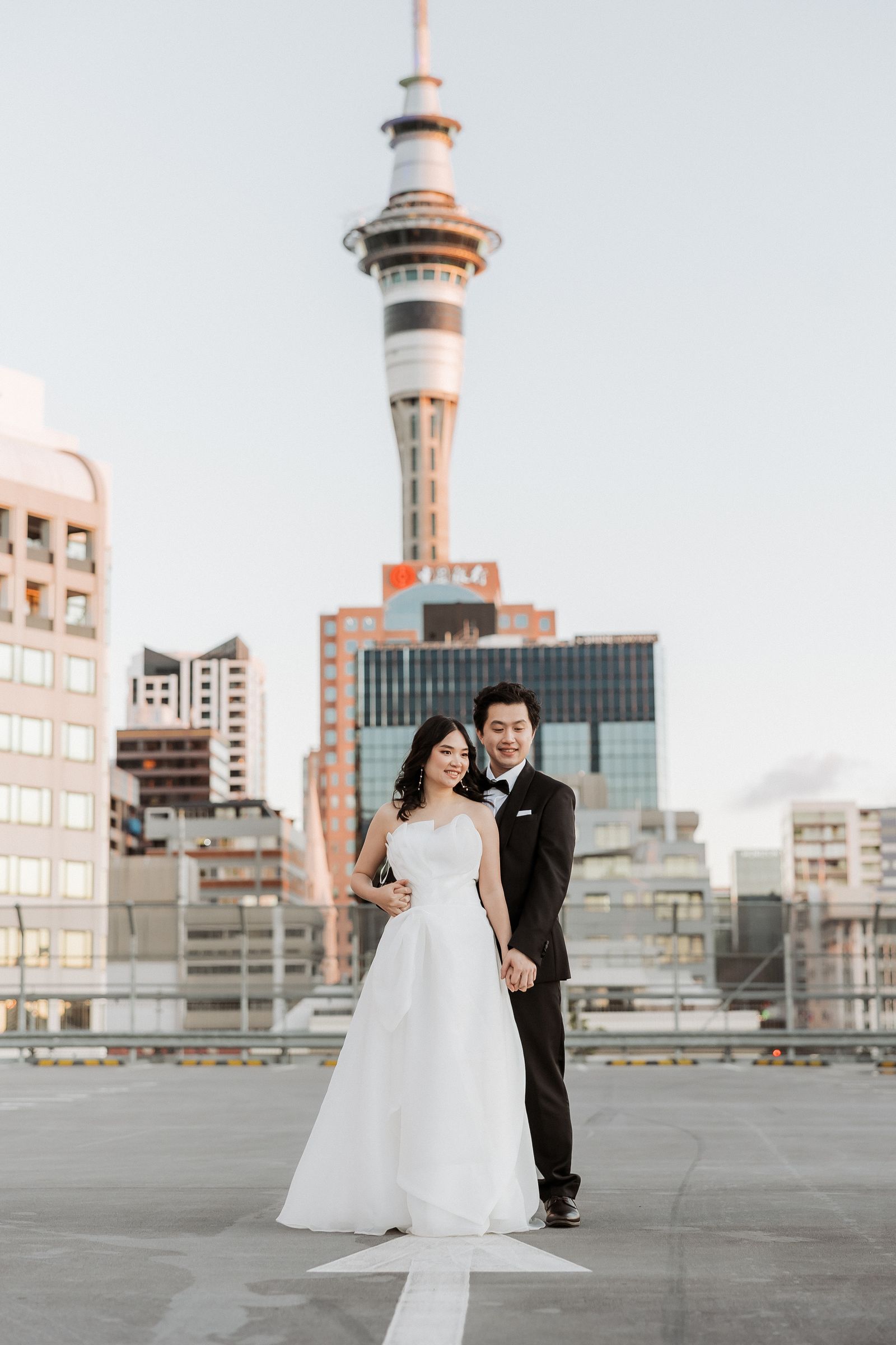 Bride and groom standing on a rooftop with the Sky Tower centred behind them