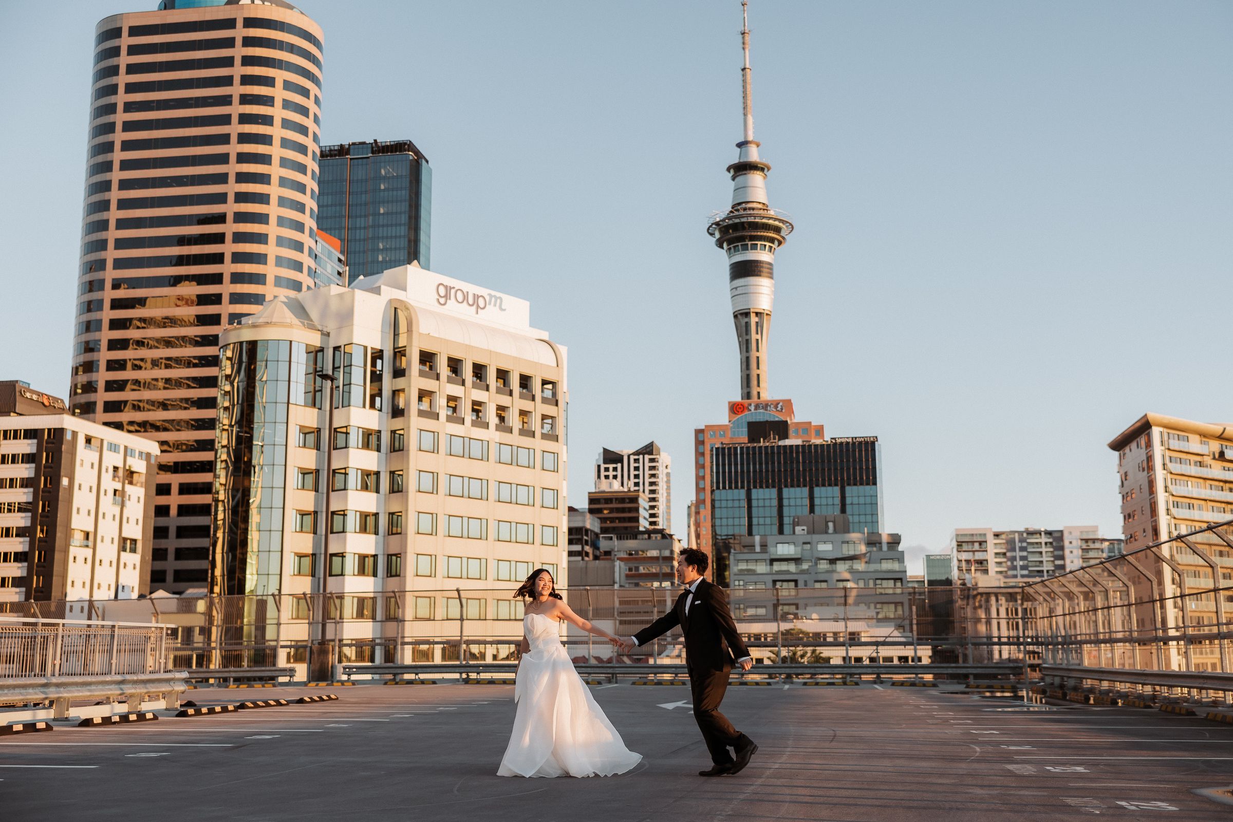 Couple walking hand in hand across a rooftop car park with the Sky Tower behind
