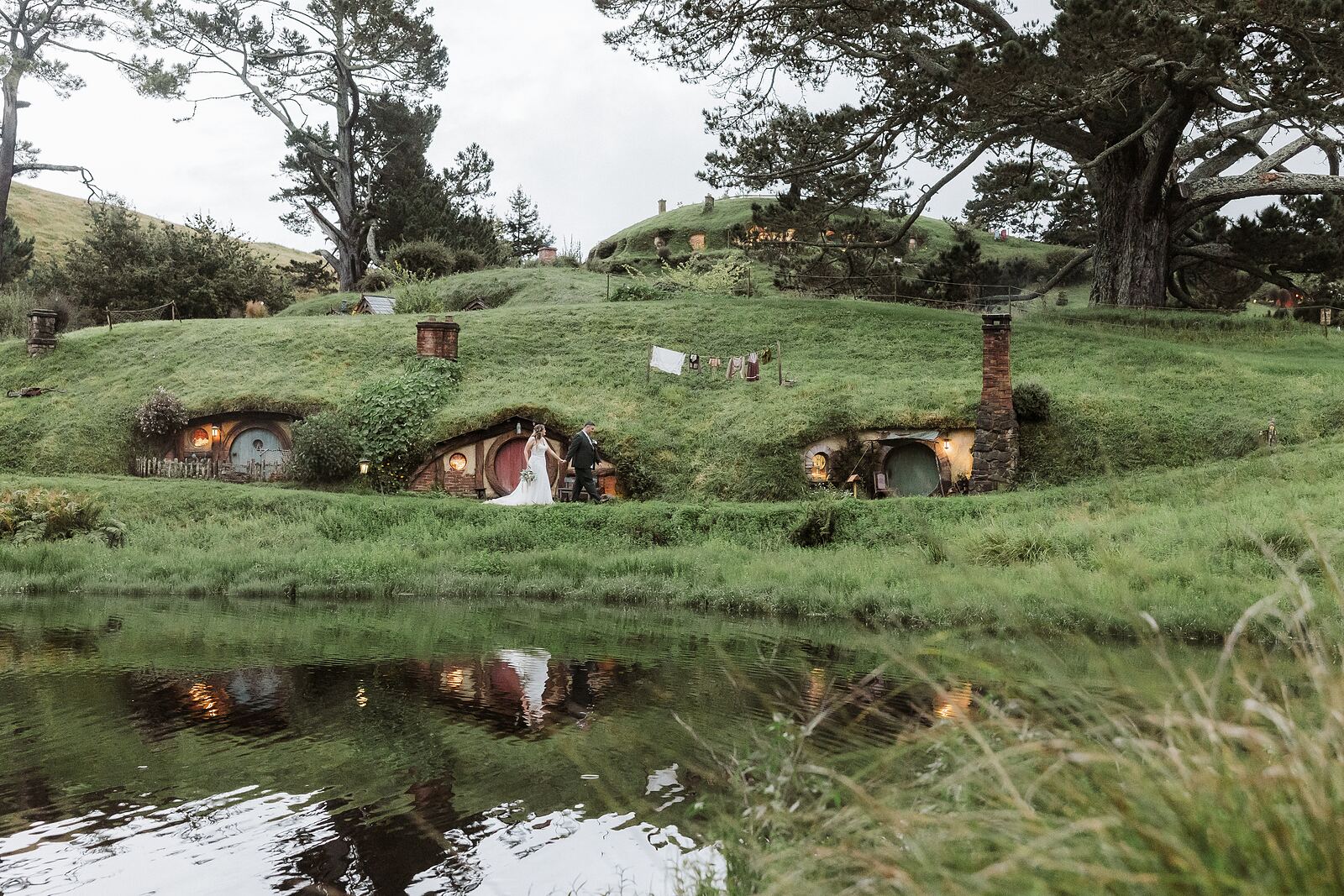 Wedding couple at dusk beside the pond and hobbit holes at Hobbiton, Matamata, Waikato