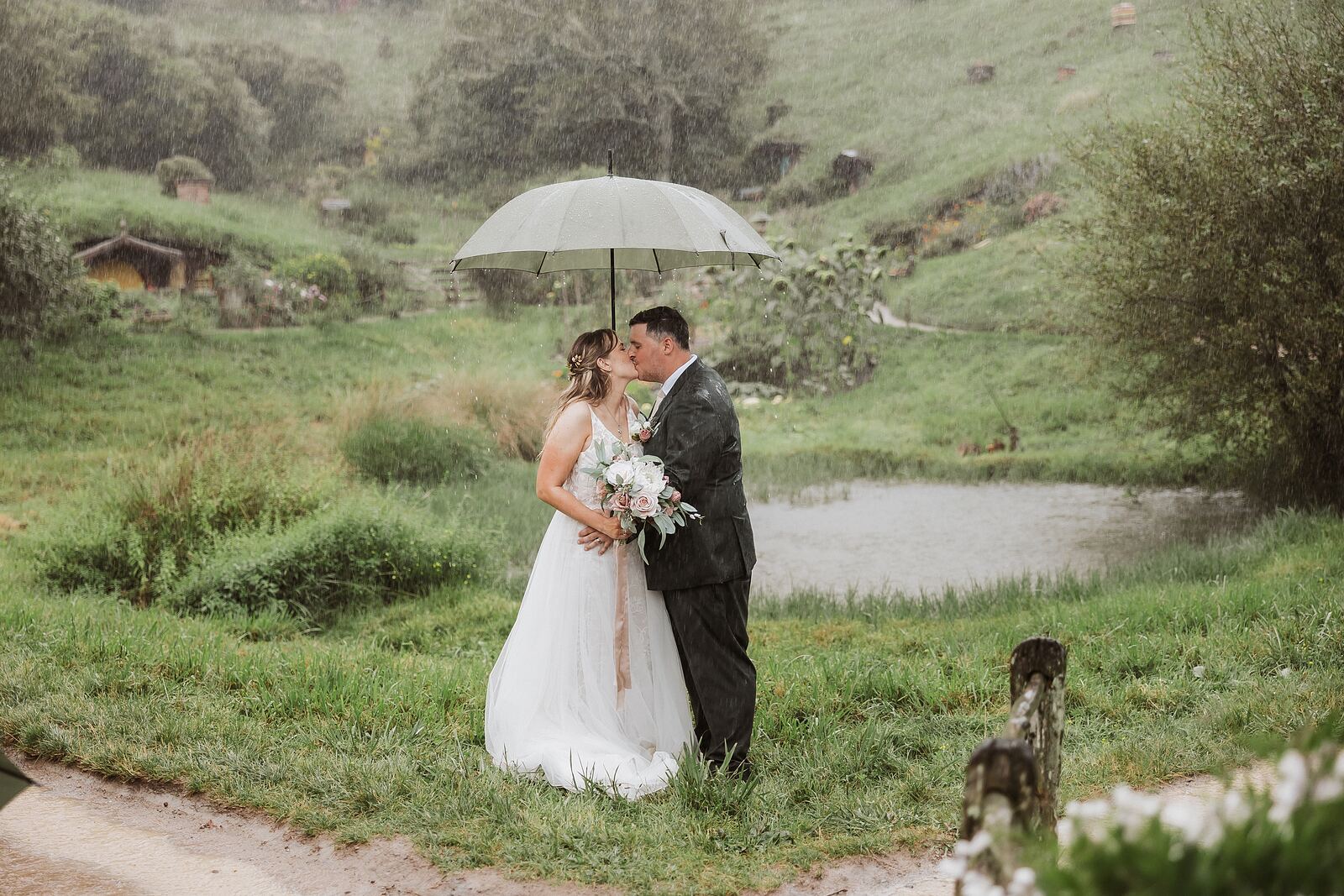 Couple under an umbrella by the pond at Hobbiton in the rain