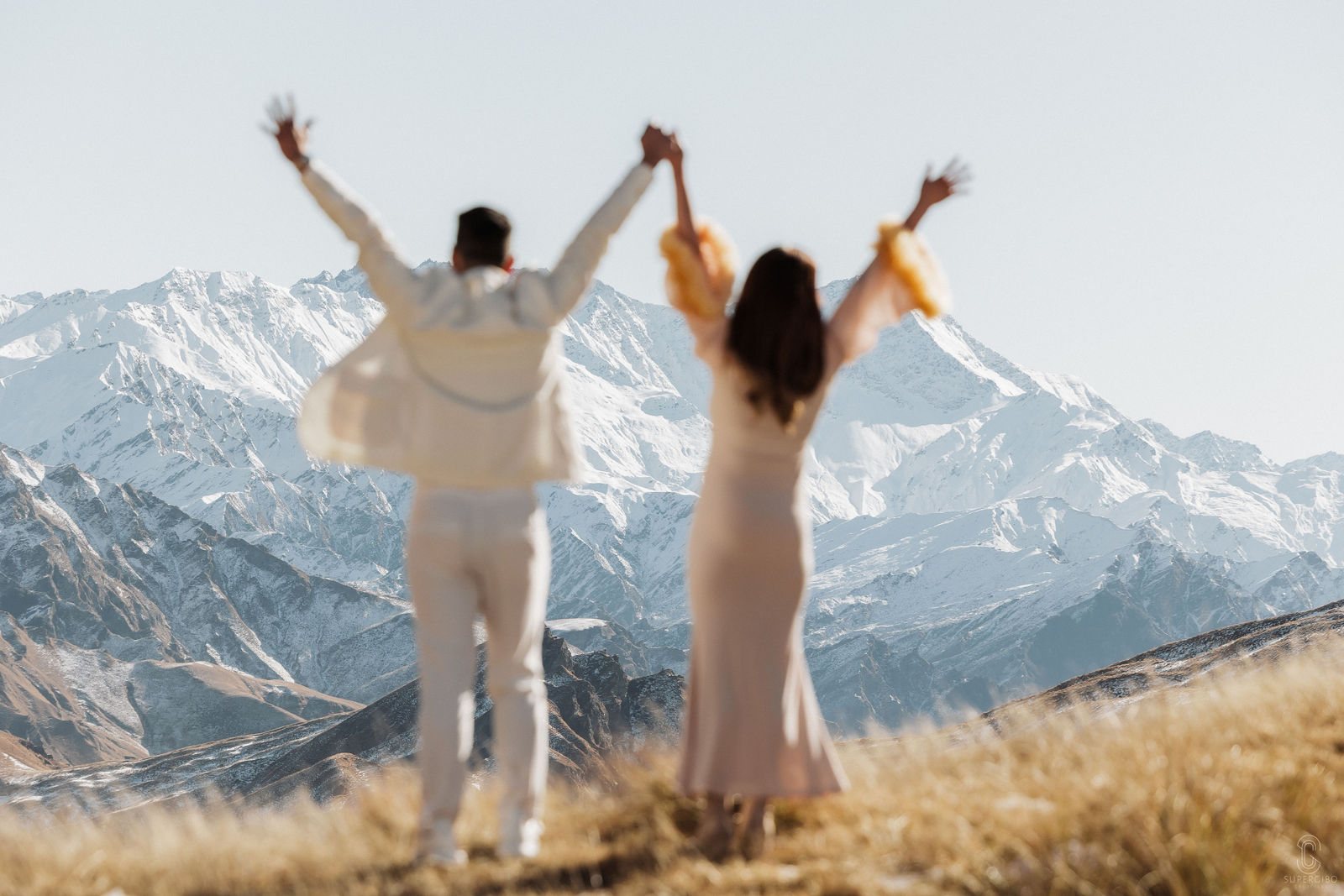 Couple with arms raised on a snowy ridge above Queenstown