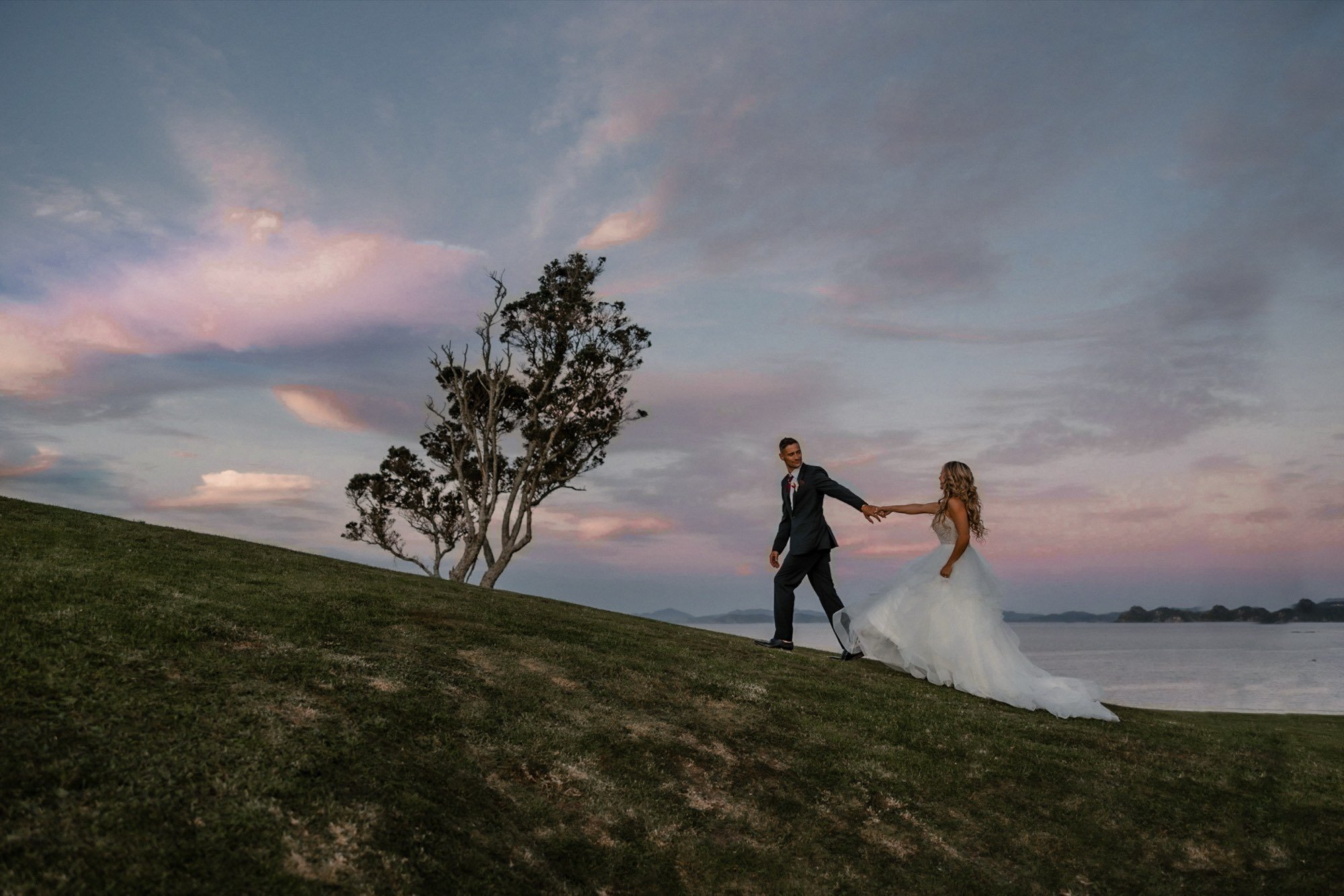 Couple walking a farm ridge at pink sunset, New Zealand wedding
